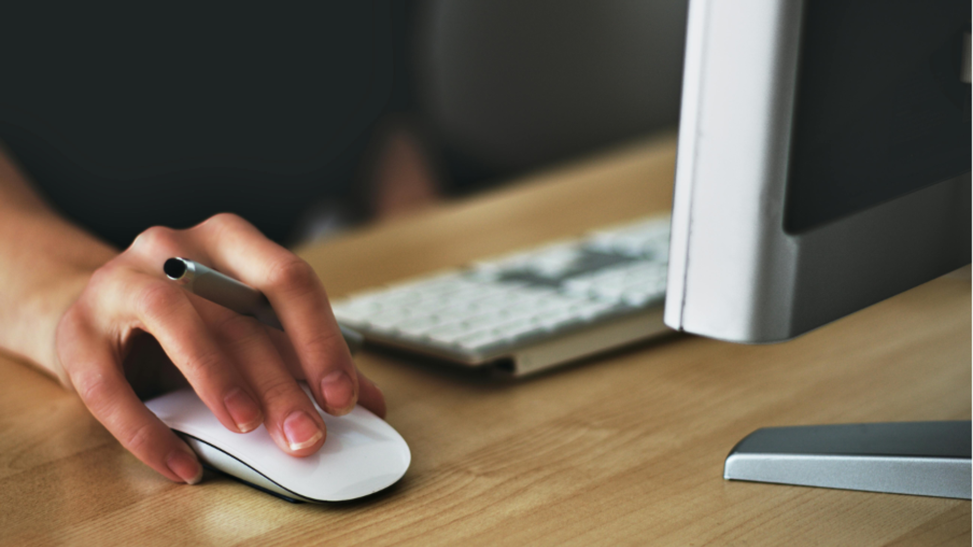 hand on a mouse with keyboard in background on a desk