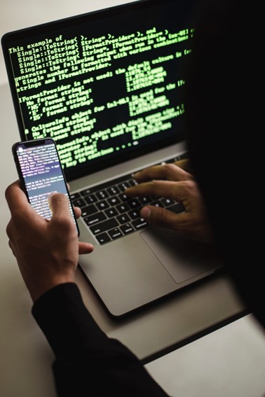 hacker writing code while holding a phone with code on it