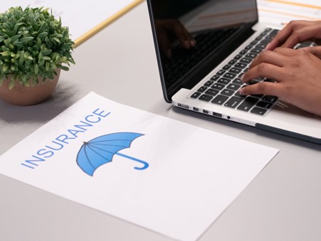 person on laptop with paper that has blue ubrealla and says insurance